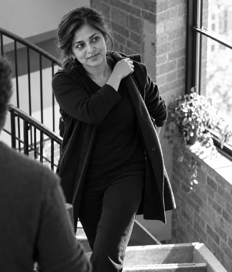 Priya pulling on her coat on an office stairwell after a client meeting.
